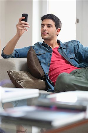 Man reclining on a couch and using a mobile phone Stock Photo - Premium Royalty-Free, Code: 6108-06166860