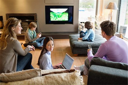 Famille à l'aide de gadgets électroniques dans une salle de séjour Photographie de stock - Premium Libres de Droits, Code: 6108-06166957