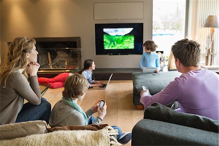 Famille à l'aide de gadgets électroniques dans une salle de séjour Photographie de stock - Premium Libres de Droits, Code: 6108-06166962