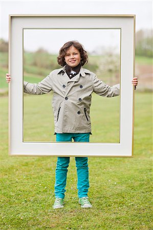 encadré - Portrait d'un garçon debout avec un frame dans un parc Photographie de stock - Premium Libres de Droits, Code: 6108-06167035