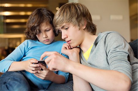 Adolescent avec son frère à l'aide d'un téléphone portable Photographie de stock - Premium Libres de Droits, Code: 6108-06167273