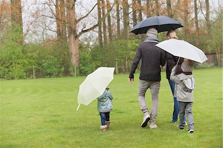 padded jacket - Family walking with umbrellas in a park Stock Photo - Premium Royalty-Free, Code: 6108-06167345