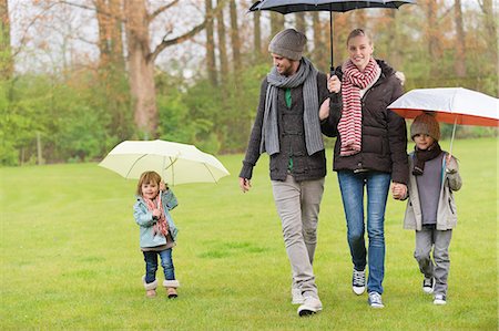 family happiness grass - Family walking with umbrellas in a park Stock Photo - Premium Royalty-Free, Code: 6108-06167366