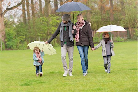 rain walk - Family walking with umbrellas in a park Stock Photo - Premium Royalty-Free, Code: 6108-06167317