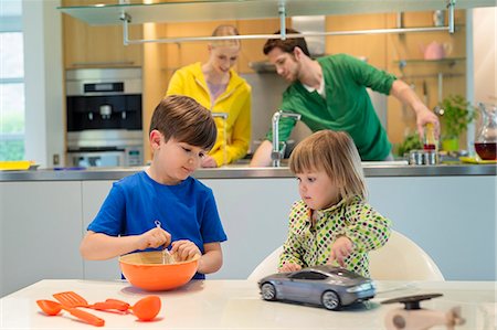 Little girl with a toy car looking at his brother cooking in the kitchen Stock Photo - Premium Royalty-Free, Code: 6108-06167565