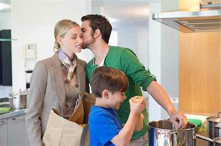 father and son cooking - Man kissing his wife returning from shopping and son cooking in the kitchen Stock Photo - Premium Royalty-Free, Code: 6108-06167577