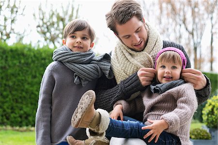 sister sits on brother laps photos - Man with his son and daughter in warm clothing in a park Stock Photo - Premium Royalty-Free, Code: 6108-06167526