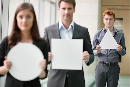 Business executives holding geometrical shaped placards in an office Stock Photo - Premium Royalty-Free, Code: 6108-06167894
