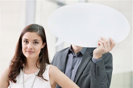 people and speech bubbles - Portrait of a businesswoman with her colleague holding speech bubble in the background Stock Photo - Premium Royalty-Free, Code: 6108-06167896