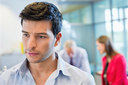 simsearch:6108-06167979,k - Male executive thinking in an office with his colleagues discussing in the background Stock Photo - Premium Royalty-Free, Code: 6108-06167973