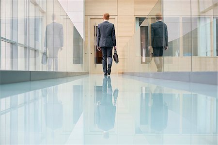 Rear view of a businessman walking in an office corridor Stock Photo - Premium Royalty-Free, Code: 6108-06168078