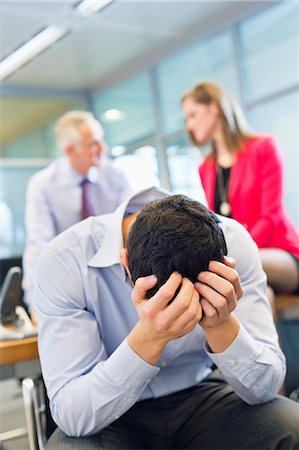 simsearch:6108-06167979,k - Male executive looking worried in an office with his colleagues discussing in the background Stock Photo - Premium Royalty-Free, Code: 6108-06168014