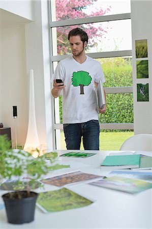 Man using a mobile phone with environment related posters in front of him on a table Stock Photo - Premium Royalty-Free, Code: 6108-06168125