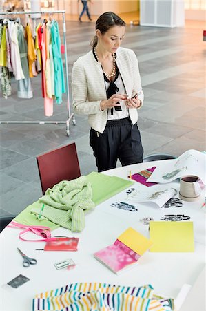 small business office person alone - Female fashion designer text messaging in an office Stock Photo - Premium Royalty-Free, Code: 6108-06168267