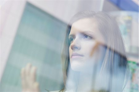 Businesswoman looking through the glass of a window Stock Photo - Premium Royalty-Free, Code: 6108-06168293