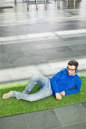 Businessman relaxing on grass and listening to music in an office lobby Stock Photo - Premium Royalty-Free, Code: 6108-06168335