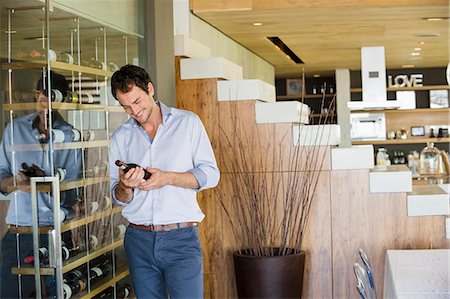 Smiling man looking at a wine bottle Stock Photo - Premium Royalty-Free, Code: 6108-06904575