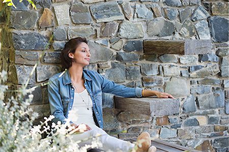 Woman leaning against a stone wall and day dreaming Stock Photo - Premium Royalty-Free, Code: 6108-06904774