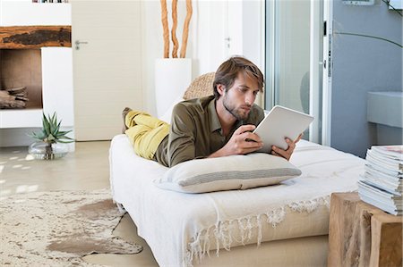 Man using a digital tablet on the bed Stock Photo - Premium Royalty-Free, Code: 6108-06904870
