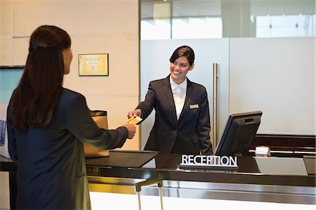 Businesswoman paying with a credit card at the hotel reception counter Stock Photo - Premium Royalty-Free, Code: 6108-06905009