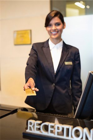 simsearch:6108-06906740,k - Receptionist holding a credit card and smiling at the hotel reception counter Stock Photo - Premium Royalty-Free, Code: 6108-06905013