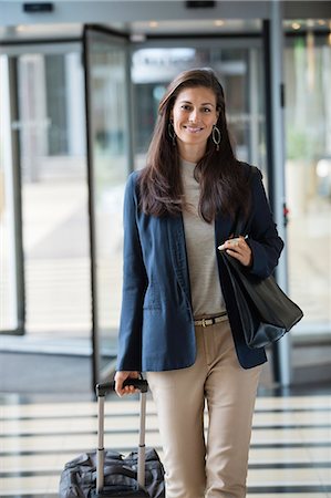 portraits and one person and smiling not black not kids not babies not teens not illustration - Businesswoman pulling a suitcase in a hotel lobby Stock Photo - Premium Royalty-Free, Code: 6108-06905024