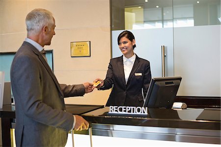 Businessman paying with a credit card at the hotel reception counter Stock Photo - Premium Royalty-Free, Code: 6108-06905034