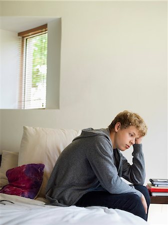 Teenage boy sitting on the bed and thinking Stock Photo - Premium Royalty-Free, Code: 6108-06905273