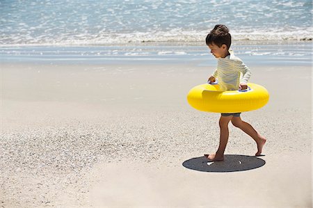 Boy holding an inflatable ring and walking on the beach Stock Photo - Premium Royalty-Free, Code: 6108-06905283