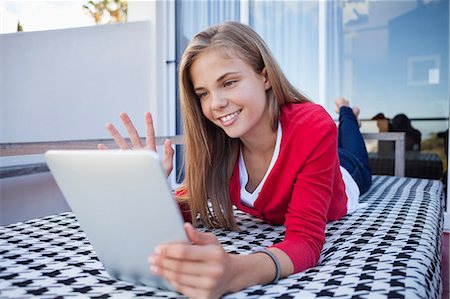 Girl lying on the bed and video chatting on a digital tablet Stock Photo - Premium Royalty-Free, Code: 6108-06905223