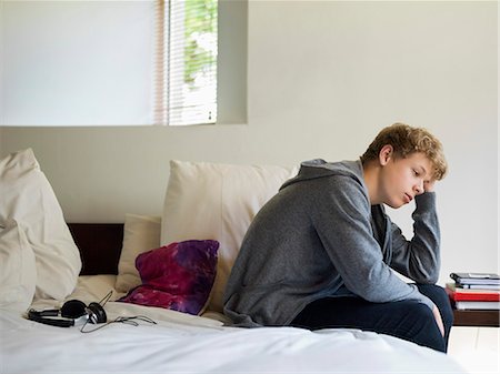 Teenage boy sitting on the bed and thinking Stock Photo - Premium Royalty-Free, Code: 6108-06905229