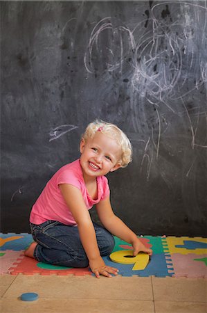 play with kid - Smiling girl playing with number puzzle in front of a blackboard Stock Photo - Premium Royalty-Free, Code: 6108-06905309