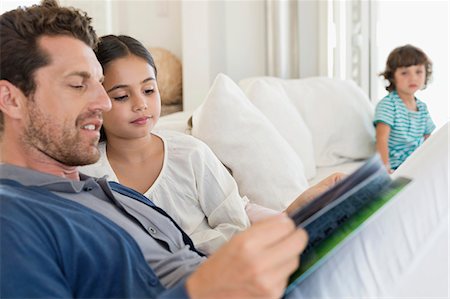 father son reading - Man reading a magazine with his daughter and his son in the background Stock Photo - Premium Royalty-Free, Code: 6108-06905583