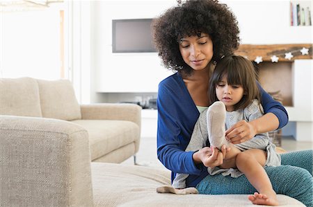 ethnic diversity - Woman putting on socks to her daughter and smiling Stock Photo - Premium Royalty-Free, Code: 6108-06905584