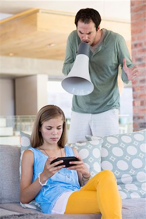 Man shouting into a megaphone at his daughter for playing video game Foto de stock - Sin royalties Premium, Código: 6108-06905627