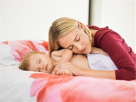 sleeping baby lying - Woman resting her head on her baby hand sleeping on the bed Stock Photo - Premium Royalty-Free, Code: 6108-06906060