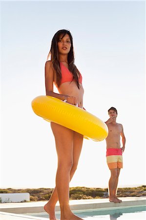 silhouette of lady walking - Woman walking with inflatable ring at the poolside with a man behind her Foto de stock - Sin royalties Premium, Código: 6108-06906296