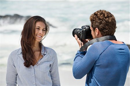 Man taking a picture of his wife with a camera on the beach Stock Photo - Premium Royalty-Free, Code: 6108-06906316