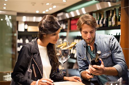 Sales clerk showing a wine bottle to a customer Photographie de stock - Premium Libres de Droits, Code: 6108-06907195