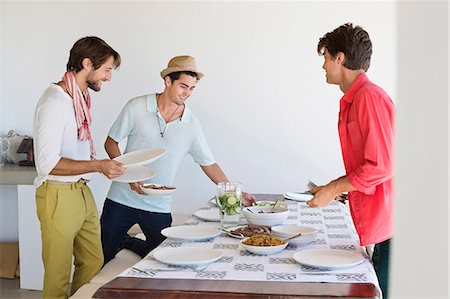 Friends arranging food on a dining table Photographie de stock - Premium Libres de Droits, Code: 6108-06907317