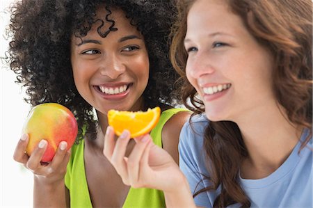 Close-up of two smiling female friends eating fruits Stock Photo - Premium Royalty-Free, Code: 6108-06907401