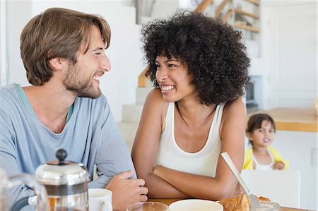 Couple smiling at a dining table with their daughter in the background Photographie de stock - Premium Libres de Droits, Code: 6108-06907631