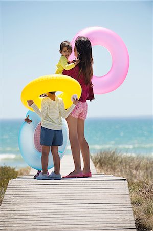 siblings at beach - Woman with her children holding inflatable rings on a boardwalk on the beach Stock Photo - Premium Royalty-Free, Code: 6108-06907717