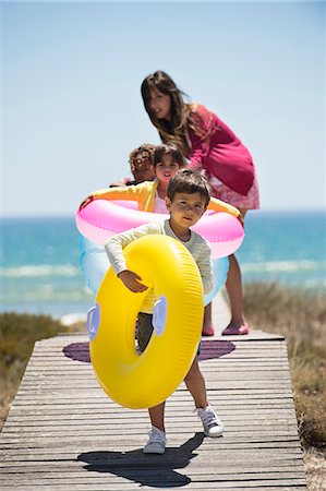 simsearch:6108-06907544,k - Woman with her children holding inflatable rings on a boardwalk on the beach Stock Photo - Premium Royalty-Free, Code: 6108-06907718