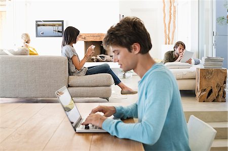 Man using a laptop with his friends using electronic gadgets in background Stock Photo - Premium Royalty-Free, Code: 6108-06907729
