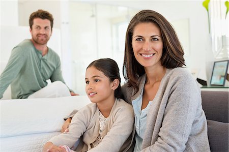 Woman sitting with her daughter and her husband in the background Stock Photo - Premium Royalty-Free, Code: 6108-06907893