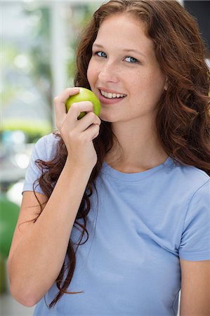 Woman eating a green apple and smiling Fotografie stock - Premium Royalty-Free, Codice: 6108-06907801