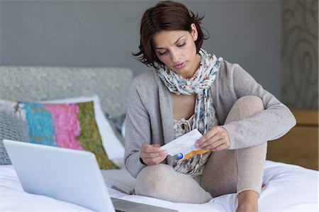 Woman looking at a paper while using a laptop Stock Photo - Premium Royalty-Free, Code: 6108-06908092