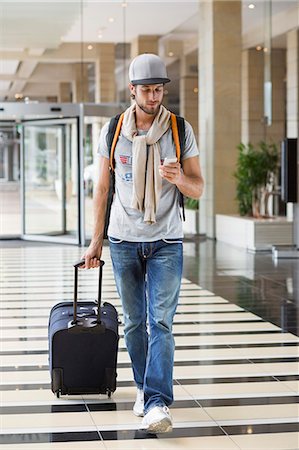 people in the airport - Man pulling his luggage at an airport and using a mobile phone Stock Photo - Premium Royalty-Free, Code: 6108-06908119