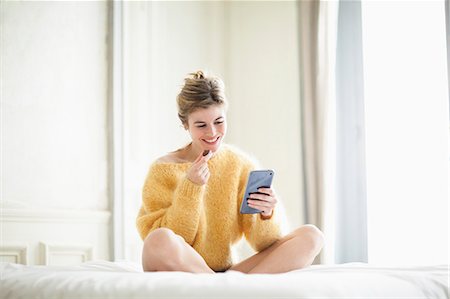 Woman using phone and eating chocolate on bed Photographie de stock - Premium Libres de Droits, Code: 6108-07969521